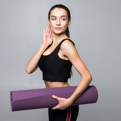 young-pretty-woman-holding-yoga-mattress-before-exercises-isolated-gray-wall_231208-1022