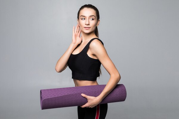 young-pretty-woman-holding-yoga-mattress-before-exercises-isolated-gray-wall_231208-1022